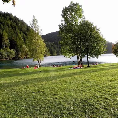 A picturesque lake surrounded by green meadows and trees. Relaxed people enjoy nature by the shore.