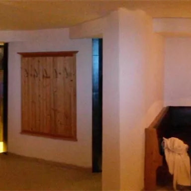 A modern living room with a wooden counter and a dining table. The walls are light and there is soft lighting in the room.