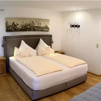 A cozy bedroom with a large bed and elegant pillows. The walls are neutral, and there is a modern picture above the bed.