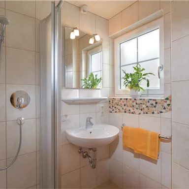A modern bathroom with a shower and sink. Bright tiles and a large window with plants create a friendly atmosphere.