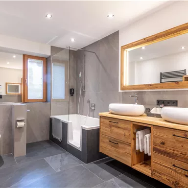 Ein modernes Badezimmer mit Holzmöbeln und zwei Waschbecken. Die Einrichtung umfasst eine Dusche und eine Badewanne, umgeben von hellen Farben und viel Licht.