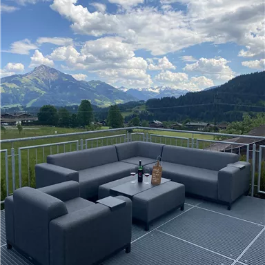 A modern terrace with a cozy seating area made of gray furniture. In the background, beautiful mountains and a clear sky can be seen.
