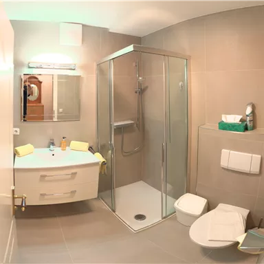 A modern bathroom with a shower, a sink, and a toilet. The walls are brightly tiled and the furnishings are simple and functional.
