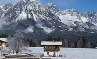 A winter landscape with snow-covered mountains and traditional wooden houses. The sky is clear and blue, ideal for winter activities.