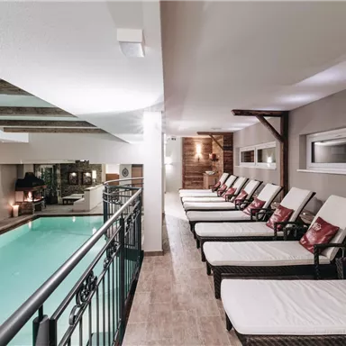 Ein entspannender Wellnessbereich mit Liegen und einem Schwimmbecken. Der Raum ist modern gestaltet und bietet eine gemütliche Atmosphäre.