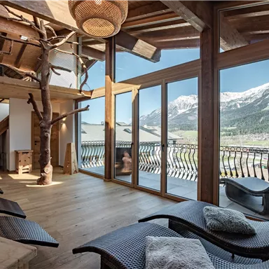Ein modernes Entspannungszimmer mit großen Fenstern und einem Blick auf die Berge. Die Möbel sind aus Holz und bieten eine gemütliche Atmosphäre.