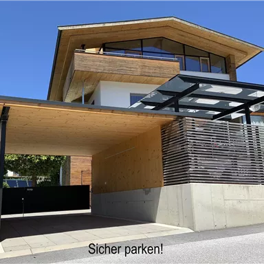 A modern house with wooden and concrete elements. The covered parking space invites for safe parking.