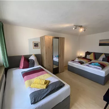 A bright bedroom with two beds and modern furniture. There is a cozy atmosphere with natural light and colored cushions.