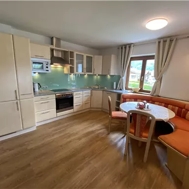 A modern kitchen with light wooden furniture and a cozy dining area. The window offers a beautiful view of nature.