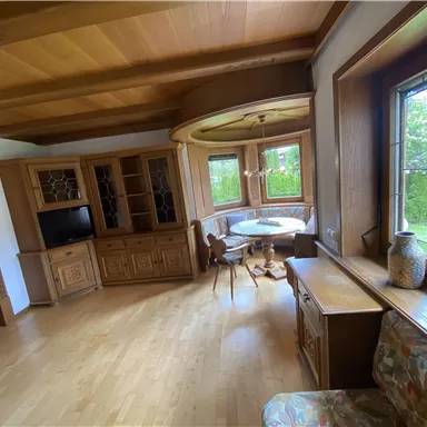 A cozy living space with wooden details and large windows. A round dining table is at the center of the room.