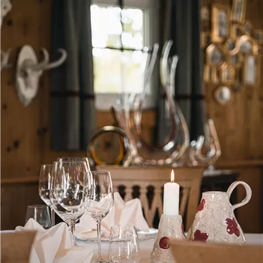 Ein stilvoll gedeckter Tisch in einem gemütlichen Raum. Das Arrangement umfasst Gläser, Servietten und eine dekorative Kanne.