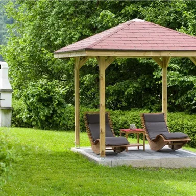 Ein Pavillon im Garten mit zwei Liegestühlen und einem kleinen Tisch. Im Hintergrund sind Bäume und ein Grill zu sehen.