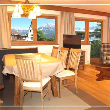 Ein gemütlicher Wohnbereich mit einem Esstisch und Stühlen. Durch die Fenster sieht man eine schöne Berglandschaft.