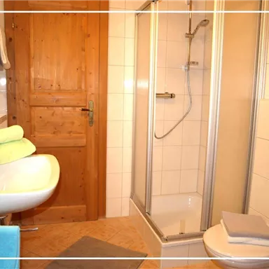 Ein modernes Badezimmer mit einer Dusche und einem Waschbecken. Auf dem Waschbecken liegen farbige Handtücher, und die Wände sind hell gefliest.