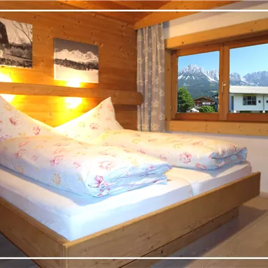 Ein gemütliches Schlafzimmer mit Holzverkleidung und großen Fenstern. Die Berge sind im Hintergrund sichtbar und das Bett ist mit blauen und floral bedruckten Decken ausgestattet.