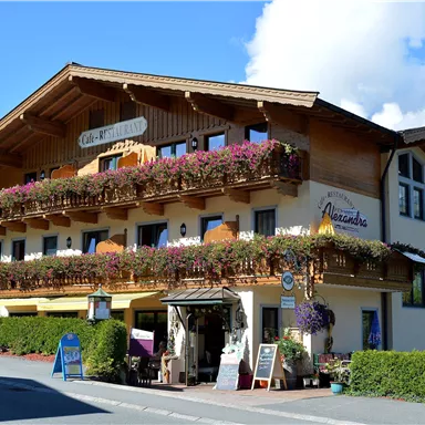 Ein schönes, traditionelles Haus mit einem Balkon voller Blumen. Die Fassade ist hell und einladend, umgeben von gepflegtem Grün.