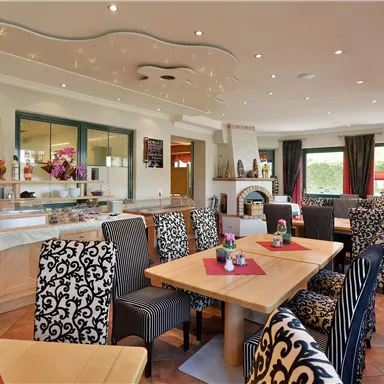 Ein gemütlicher Speisesaal mit eleganten Möbeln und schönen Tischdekorationen. Große Fenster lassen viel Licht herein und schaffen eine einladende Atmosphäre.