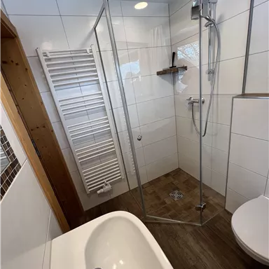A modern bathroom with a glass shower cubicle and a bathtub. The walls are tiled in bright colors, and there is a towel warmer.