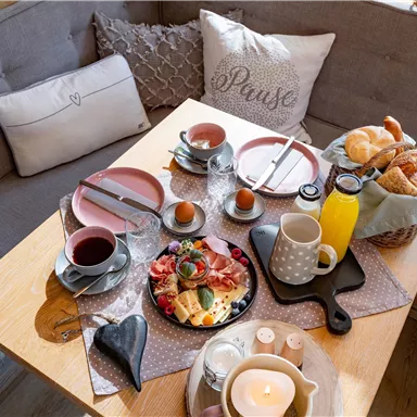 Ein hübsches Frühstücksarrangement auf einem Tisch mit verschiedenen Speisen und Getränken. Der Tisch ist liebevoll gedeckt und es gibt frisches Brot, Obst und Tee.