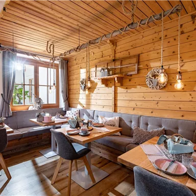 Ein gemütliches Restaurant mit Holzverkleidung und warmem Licht. Die Tische sind liebevoll gedeckt und die Fenster bieten einen Blick nach draußen.