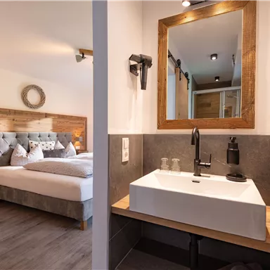 Ein modernes Badezimmer mit einem eleganten Waschbecken und einem großen Spiegel. Im Hintergrund ist ein gemütliches Schlafzimmer zu sehen.