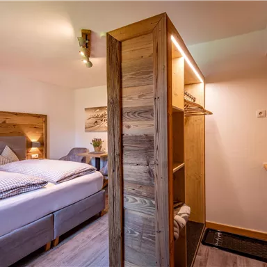 Ein gemütliches Schlafzimmer mit einem Doppelbett und warmen Holzmöbeln. Ein Kleiderschrank und dekorative Elemente schaffen eine einladende Atmosphäre.