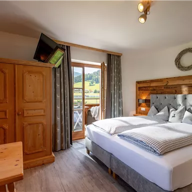 Ein gemütliches Schlafzimmer mit einem großen Bett und Holzmöbeln. Das Zimmer hat einen Balkon mit Blick auf die Landschaft.