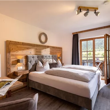 Ein gemütliches Schlafzimmer mit einem großen Bett und holzigen Akzenten. Die Fenster bieten einen Blick auf die Natur und lassen viel Licht herein.