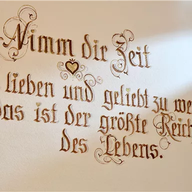 Ein schön gestalteter Schriftzug an der Wand. Er lautet: "Nimm dir Zeit zu lieben und geliebt zu werden, das ist der größte Reichtum des Lebens."