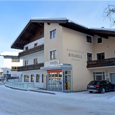 Ein gemütliches Gebäude im Schnee, das als Pension dient. Die Umgebung ist winterlich mit schneebedeckten Straßen und Bäumen.