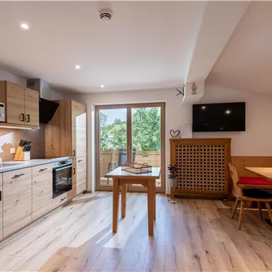 Eine moderne Küche mit Holzschränken, Herd und Mikrowelle. Der Essbereich ist gemütlich mit einer roten Sitzbank und einem Tisch.