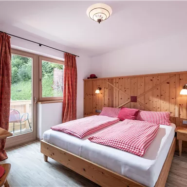 Ein gemütliches Schlafzimmer mit einem Doppelbett und Holzverkleidung. Große Fenster lassen viel Licht herein und bieten einen schönen Blick ins Grüne.