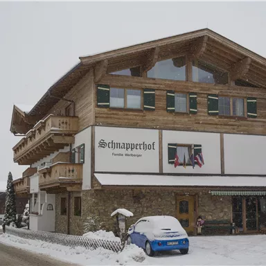 Ein charmantes Holzhaus im Schnee mit einem einladenden Schild. Die Umgebung ist winterlich und ruhig, mit verschneiten Bäumen.