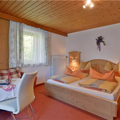 Ein gemütliches Schlafzimmer mit Holzvertäfelung, einem großen Bett und einem kleinen Tisch. Das Zimmer hat Fenster mit Vorhängen und warme Farbgestaltung.