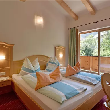 Ein gemütliches Schlafzimmer mit zwei Betten und bunten Kissen. Große Fenster bieten einen Blick auf die Natur draußen.