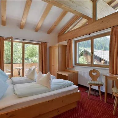 Ein gemütliches Schlafzimmer mit zwei Betten und Holzdekor. Große Fenster sorgen für viel Tageslicht und einen Blick nach draußen.