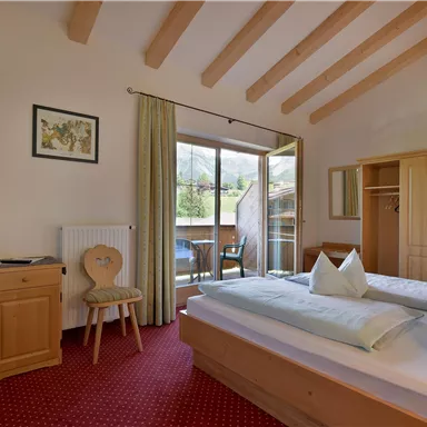 Ein gemütliches Zimmer mit zwei Betten, Holzdekor und einem Balkon. Es gibt einen Schreibtisch und einen Fernseher an der Wand.