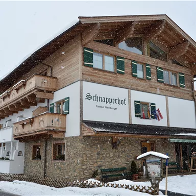 Ein traditionelles Holzgebäude mit mehreren Balkonen, umgeben von Schnee. Der Name "Schnapperhof" ist an der Wand angebracht.
