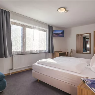 A cozy hotel room with a double bed, an armchair, and a table. Large windows provide plenty of daylight.