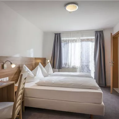 A cozy room with two single beds and a desk. The window lets in a lot of daylight.