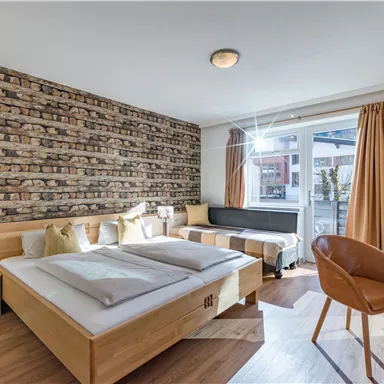 Ein modernes Zimmer mit einem Doppelbett und Holzfußboden. Die Wand ist mit Ziegelsteinen verkleidet und ein Fenster lässt viel Licht herein.