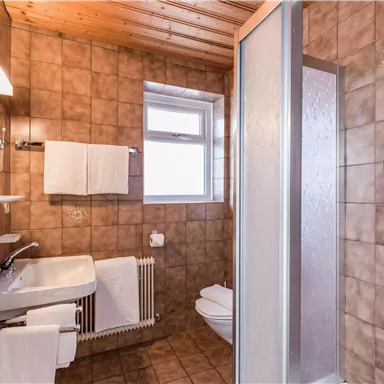 Ein modernes Bad mit Fliesen in Erdtönen und Holzdecke. Es enthält eine Dusche, ein Waschbecken und frische Handtücher.