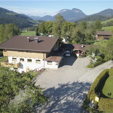 A charming house surrounded by green hills and trees. In the background, mountains are visible that create a picturesque landscape.