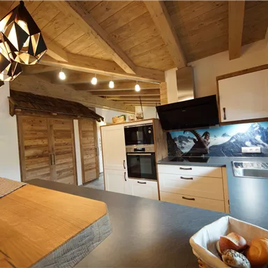 Eine moderne Küche mit Holzdecken und eleganten Lampen. Im Hintergrund ist eine beeindruckende Berglandschaft zu sehen.