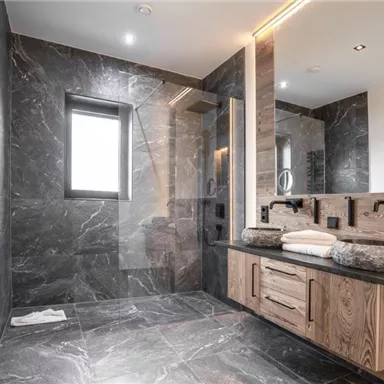 Ein modernes Badezimmer mit elegantem Marmor und Holzdetails. Es verfügt über eine Dusche und ein großes Fenster, das Licht hereinlässt.