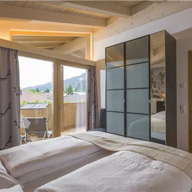 Ein modernes Schlafzimmer mit großen Fenstern und Blick auf die Berge. Die Möbel sind stilvoll und die Farben sind warm und einladend.