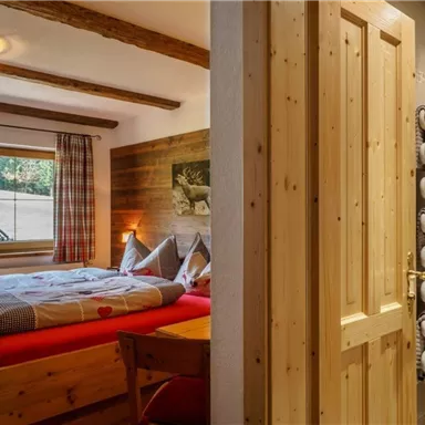 Ein gemütliches Schlafzimmer mit einem Doppelbett aus Holz und Blick auf die Landschaft. Im Hintergrund ist ein modernes Badezimmer mit Handtüchern und einem Spiegel sichtbar.