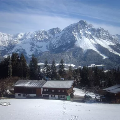 A snowy landscape with high mountains in the background. In the foreground, traditional wooden houses stand.
