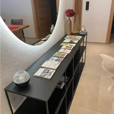 A modern hallway with a black shelf. On the shelf are several informational brochures and a vase with red flowers.