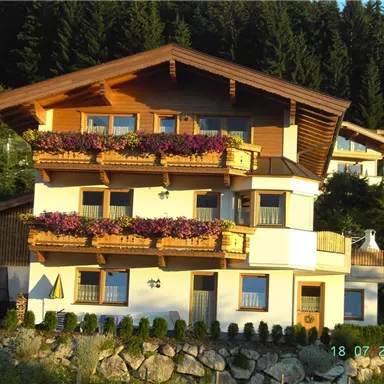 A beautiful multi-story house with a wooden roof and flower boxes. Surrounded by trees and green landscapes.